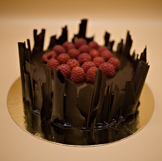 Framboos-chocoladetaart met frambozen gedecoreerd, omringd met chocoladekrullen